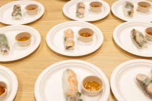 Plates of fresh spring rolls with shrimp, accompanied by small cups of dipping sauce, are arranged on a wooden table.