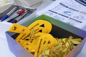 A box containing yellow ribbons with the words Drive So Others Survive and a yellow ribbon symbol. Nearby, there are pens in a white container and a stack of pamphlets with text and symbols visible.