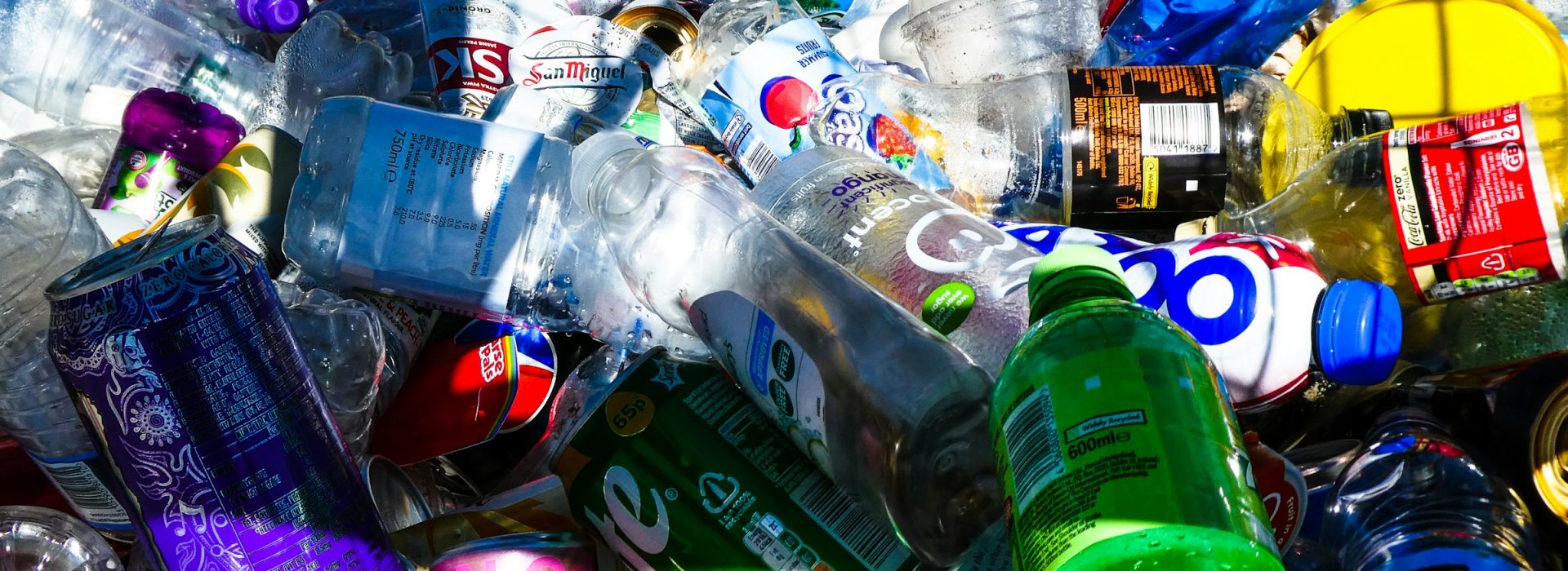 A pile of assorted plastic bottles and aluminum cans, empty and jumbled together, illuminated by sunlight, representing recyclable waste.