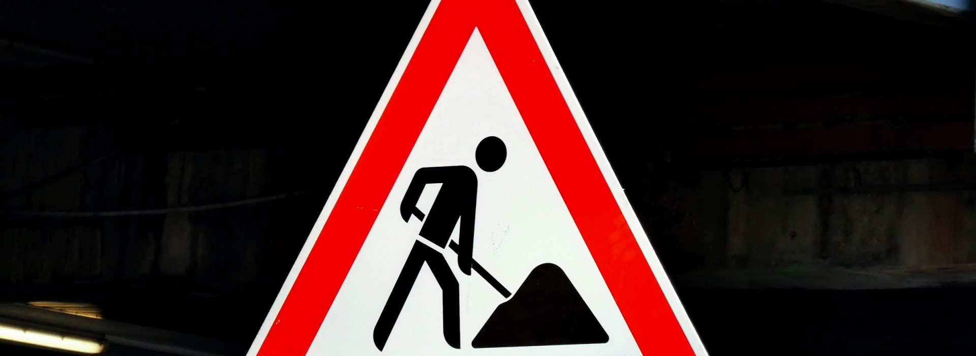 A triangular road sign with a red border shows a black silhouette of a person digging with a shovel, indicating construction or roadwork ahead.