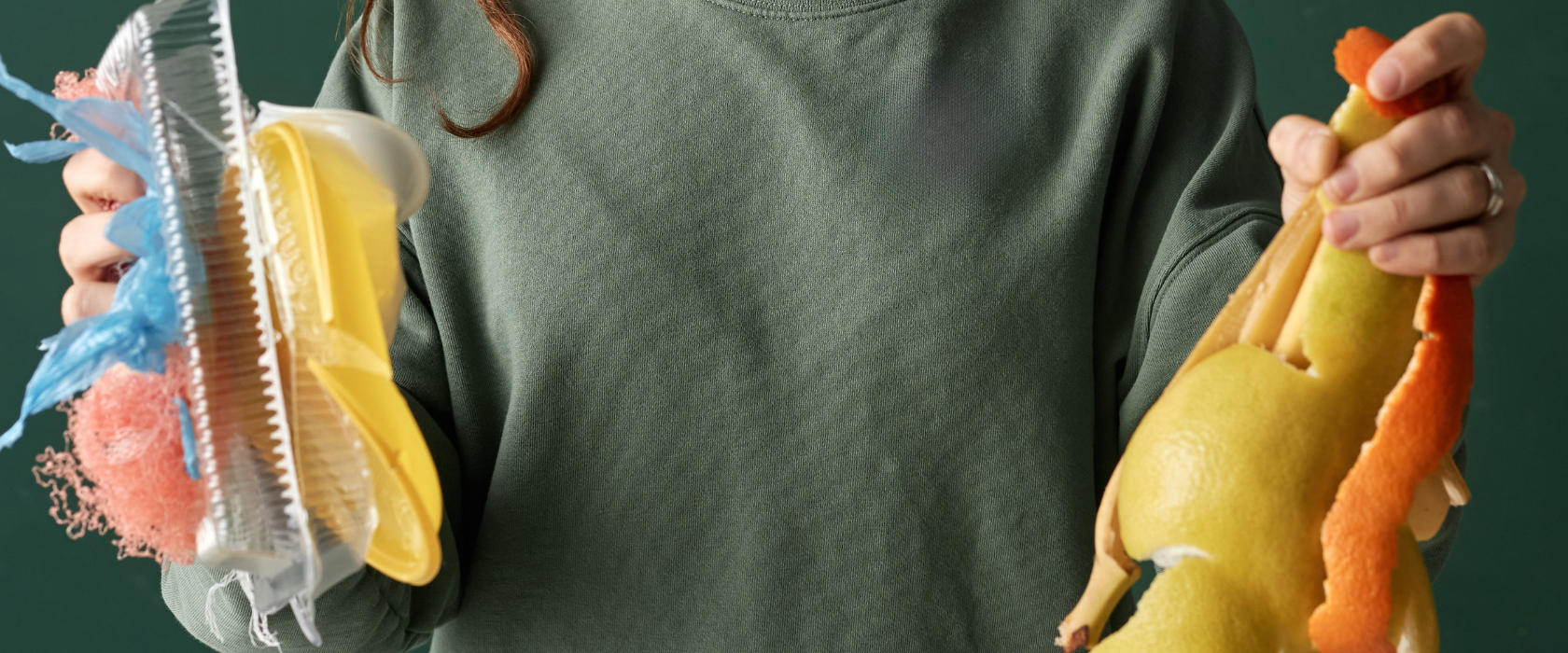 A person in a green sweatshirt holds plastic waste in one hand and fruit peels in the other, standing against a green background. Their face is partially out of frame.