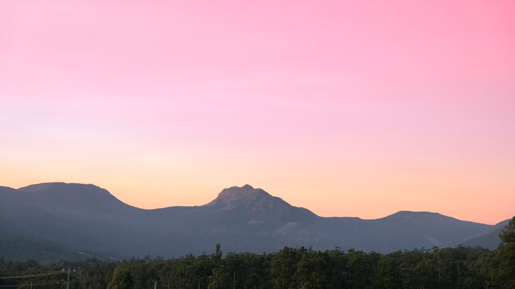 Mountain silhouette with a forest in the foreground under a vibrant pink and orange sunset sky.