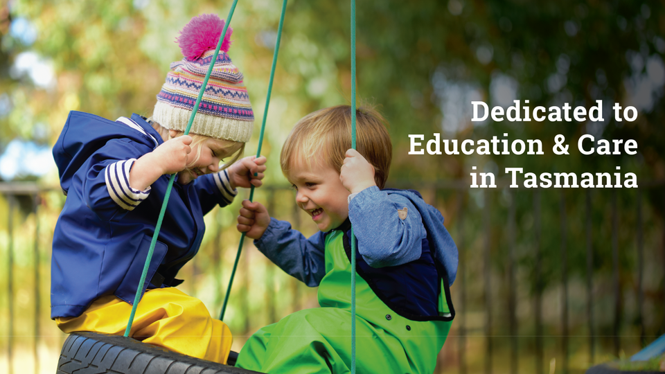 Two young children in colorful outdoor clothing smile and play together on a tire swing. Blurred trees are in the background. White text reads, “Dedicated to Education & Care in Tasmania.”.