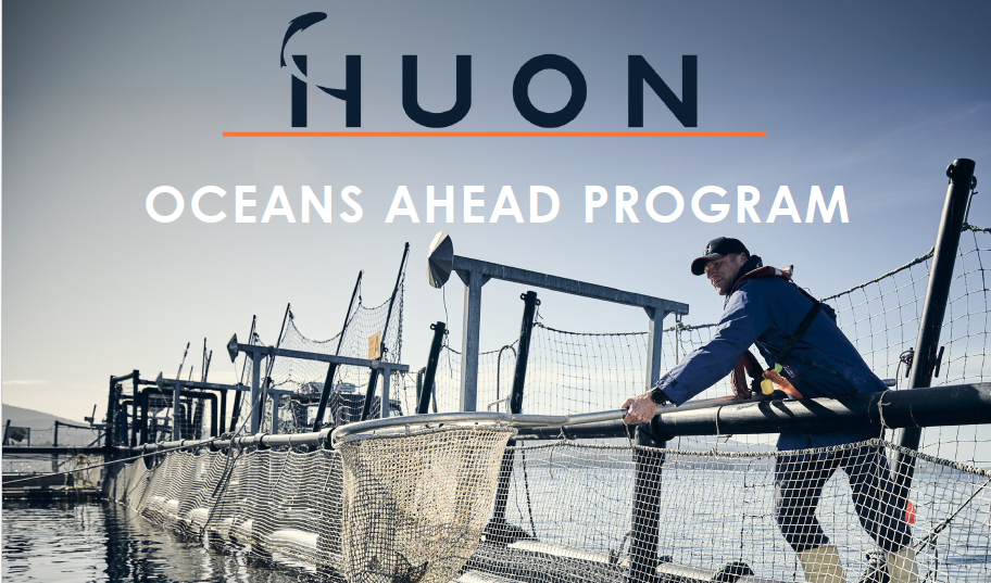 A person stands on a fish farm platform on the water under a clear sky. Text reads “HUON OCEANS AHEAD PROGRAM.”.