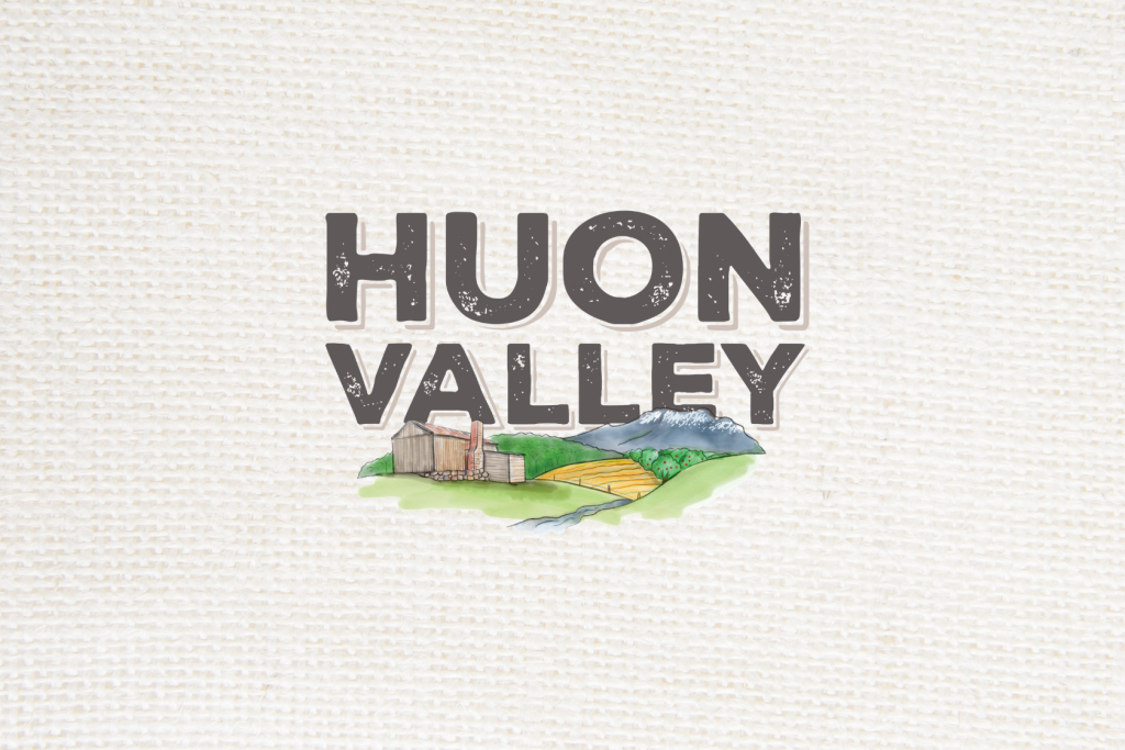 Text “HUON VALLEY” in bold letters above an illustration of a barn, green hills, yellow fields, and distant blue mountains, on a textured white background.