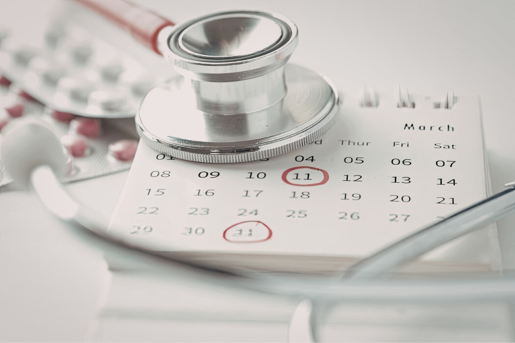 A close-up of a stethoscope resting on a calendar with the dates 11 and 31 circled in red; blurred blister packs of pills are visible in the background.